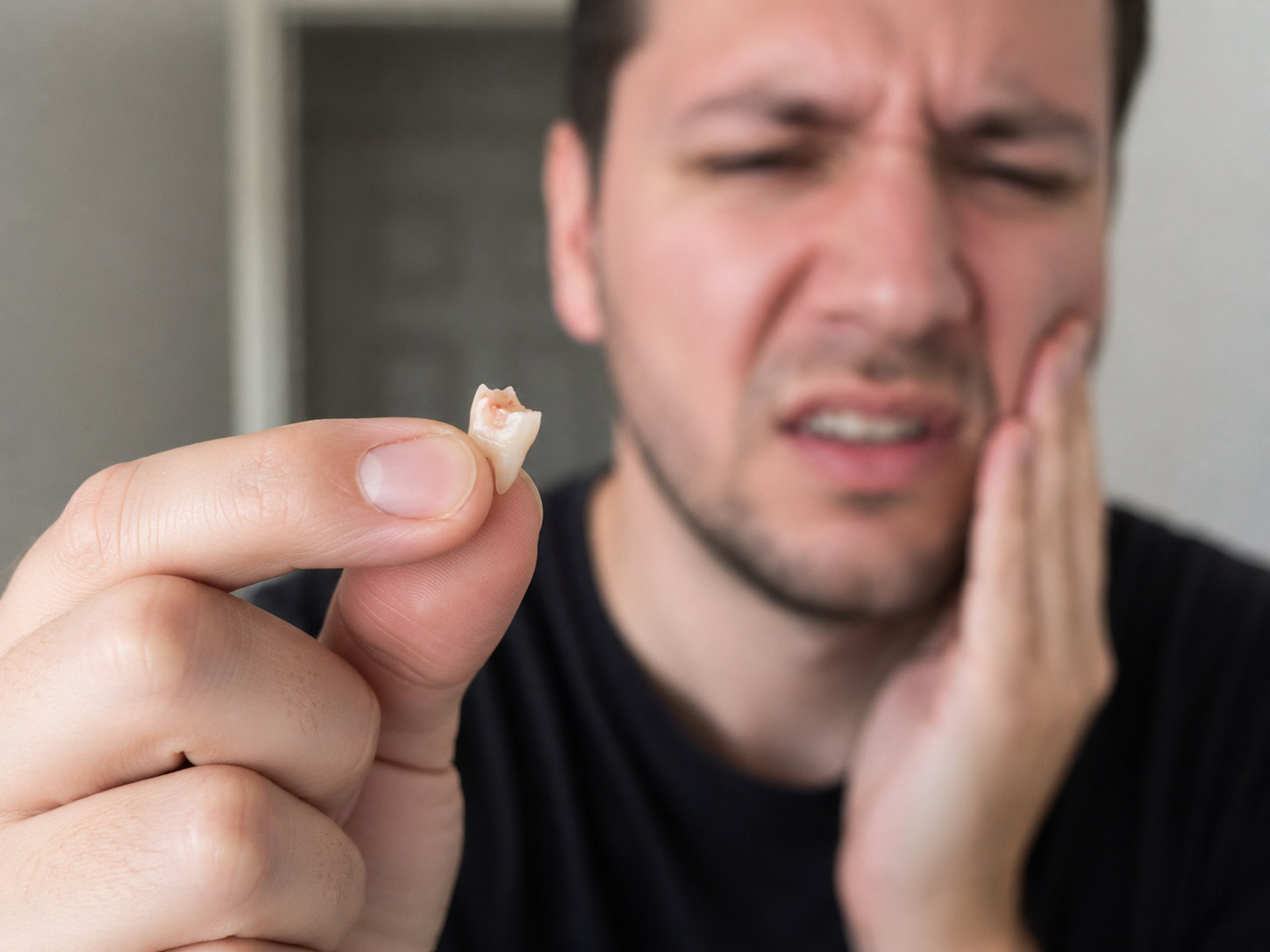 Man holding a broken tooth fragment while experiencing dental pain