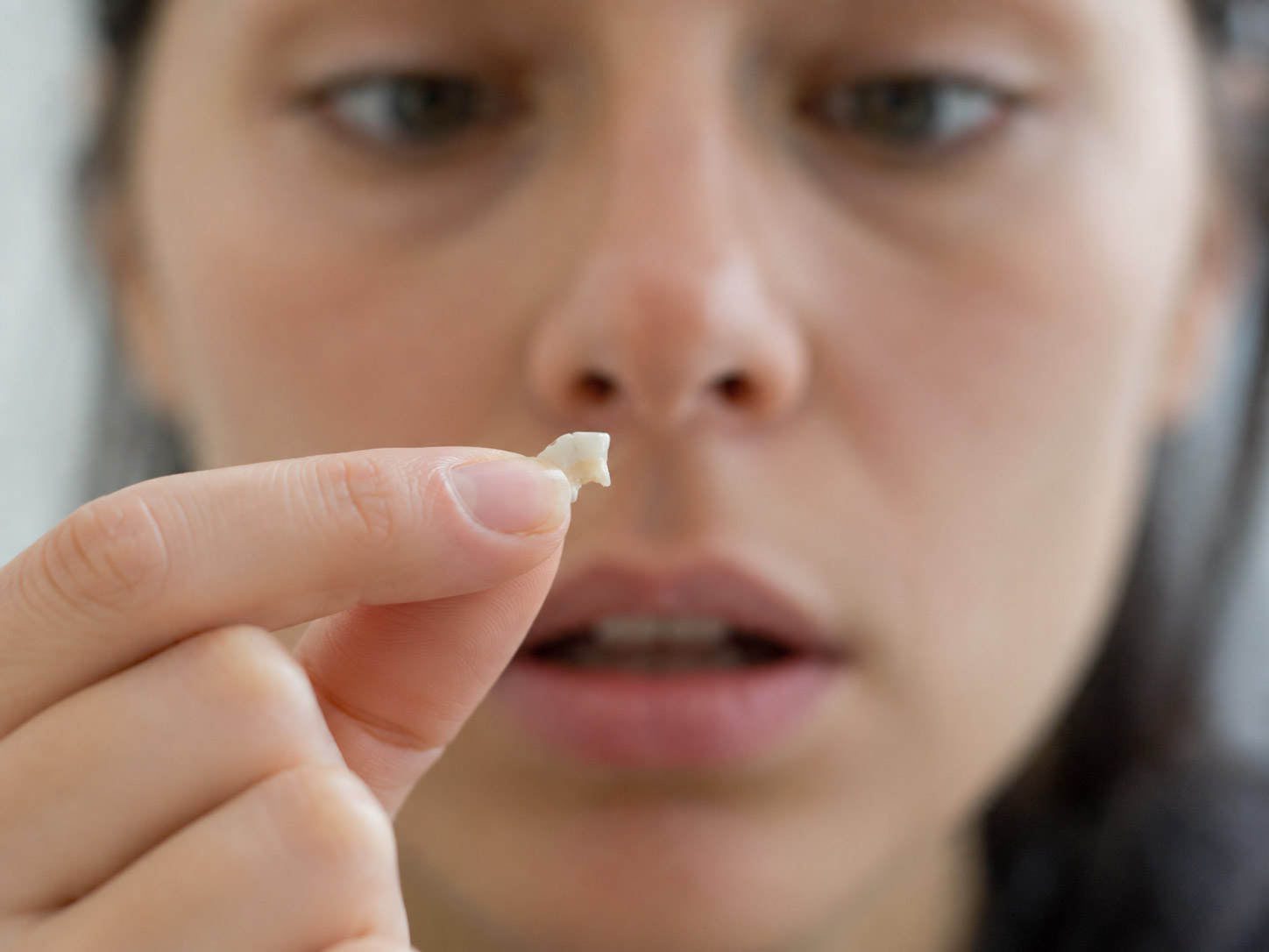 Person holding a small broken tooth fragment